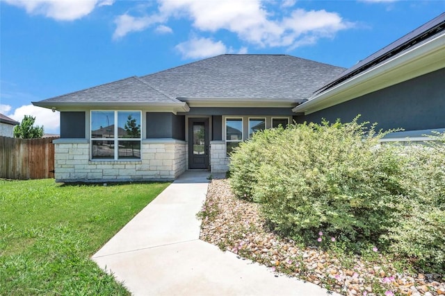 view of front of house with a front yard, a shingled roof, fence, and stone siding