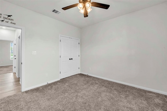 carpeted spare room with baseboards, visible vents, and ceiling fan