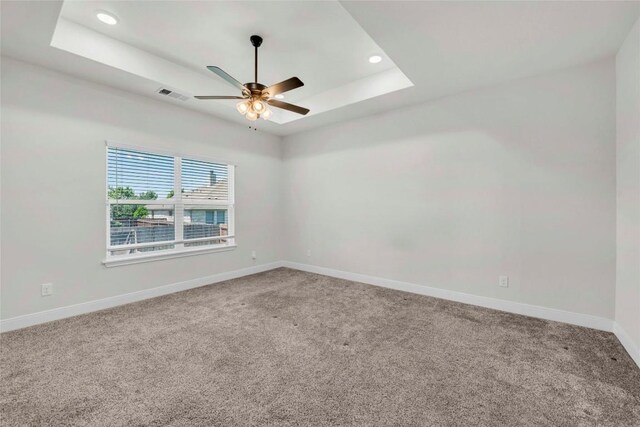 empty room with ceiling fan, a tray ceiling, visible vents, and carpet