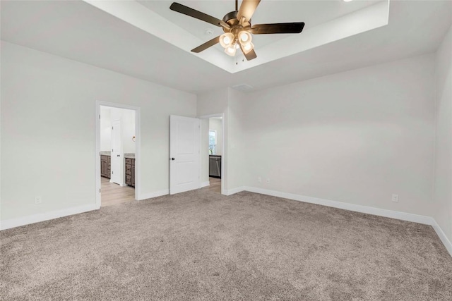 unfurnished bedroom with ensuite bathroom, light colored carpet, ceiling fan, a tray ceiling, and baseboards