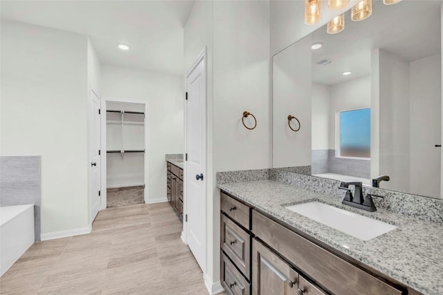 bathroom with vanity, a spacious closet, a bath, and recessed lighting