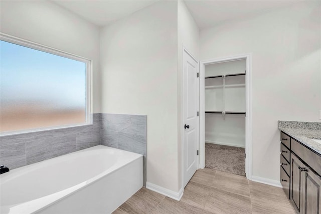 full bath featuring a bath, vanity, baseboards, and a walk in closet