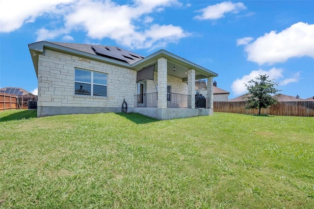 view of front facade featuring stone siding, a front yard, a fenced backyard, and roof mounted solar panels