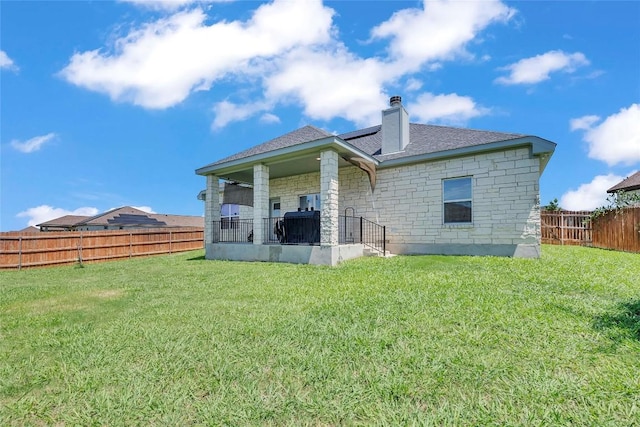 back of house with a yard, stone siding, and a fenced backyard