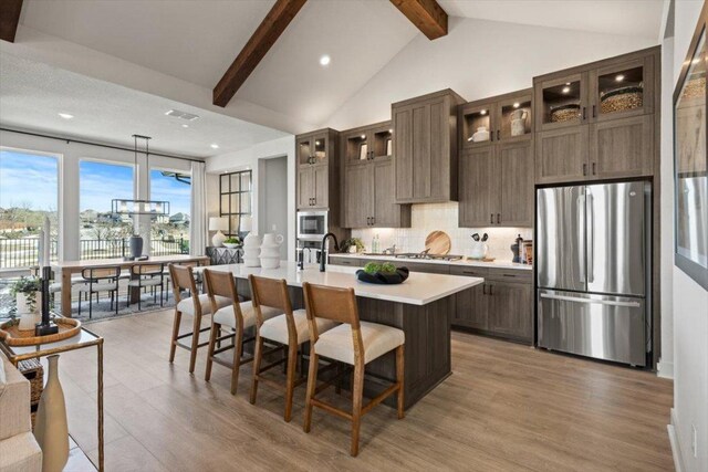 2108 Tobiano Trce, Georgetown, TX 78633 - kitchen featuring stainless steel appliances, light countertops, light wood finished floors, a center island with sink, and decorative backsplash