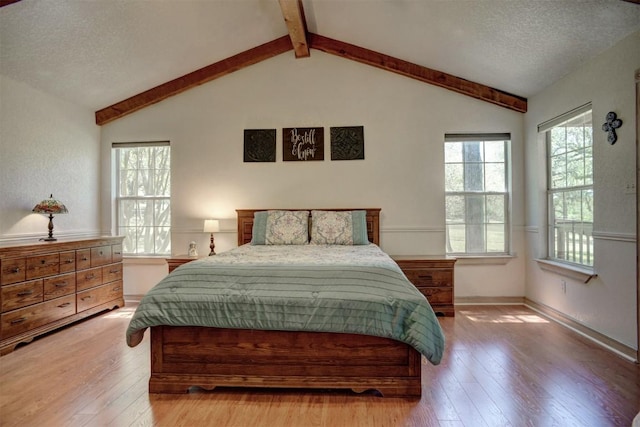 bedroom featuring lofted ceiling with beams, hardwood / wood-style flooring, baseboards, and a textured ceiling