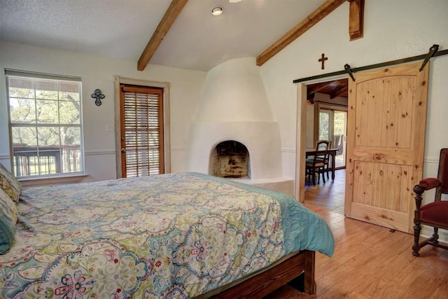 bedroom featuring lofted ceiling with beams, a barn door, multiple windows, and light wood-type flooring