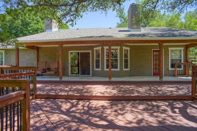 rear view of property featuring a chimney, roof with shingles, and stucco siding