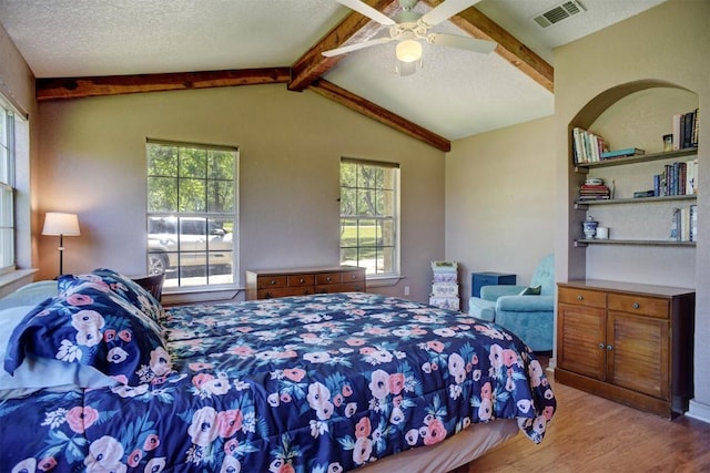 bedroom featuring vaulted ceiling with beams, wood finished floors, visible vents, and multiple windows