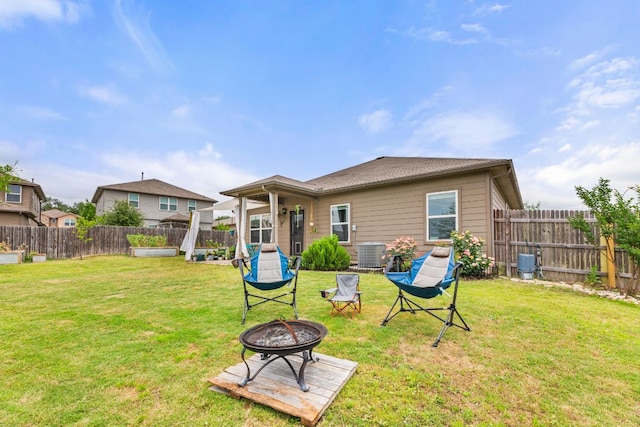 rear view of property with a fire pit, a yard, cooling unit, and a fenced backyard