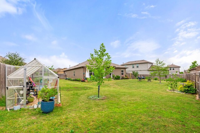 view of yard with an outdoor structure, a fenced backyard, and a greenhouse