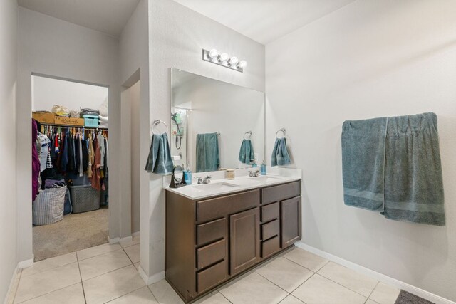 full bath with a sink, tile patterned floors, a walk in closet, double vanity, and baseboards