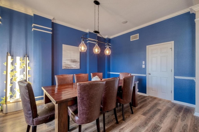 dining room with baseboards, wood finished floors, visible vents, and crown molding