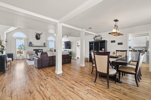 dining area with a fireplace, light wood-style flooring, visible vents, and vaulted ceiling with beams