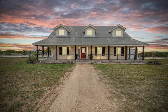 farmhouse inspired home featuring a yard, stone siding, covered porch, and fence