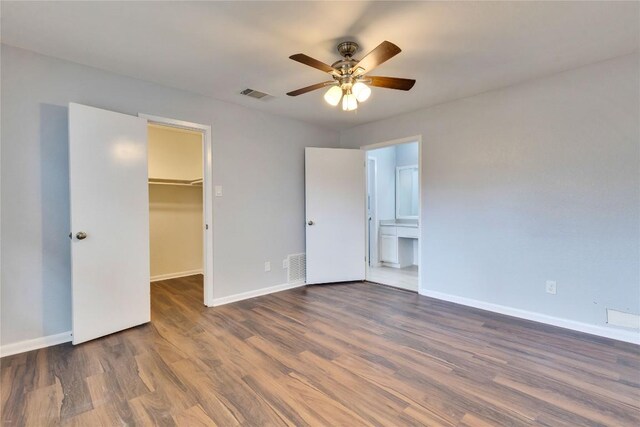 unfurnished bedroom featuring baseboards, visible vents, a spacious closet, wood finished floors, and a closet