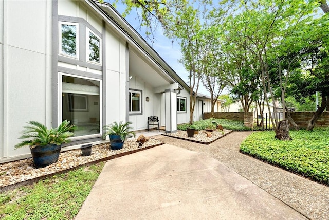 view of exterior entry with fence, board and batten siding, and a patio