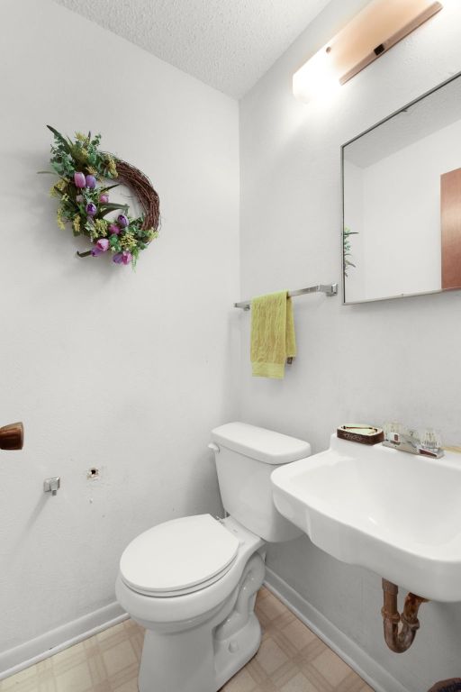 half bath featuring tile patterned floors, baseboards, a textured ceiling, and toilet