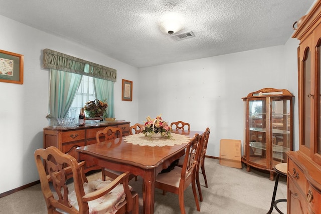 dining area featuring a textured ceiling, baseboards, visible vents, and light colored carpet