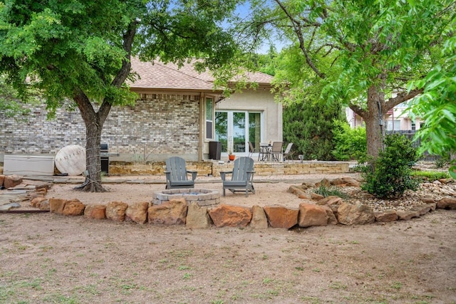 rear view of house with french doors, a fire pit, brick siding, a patio area, and a shingled roof