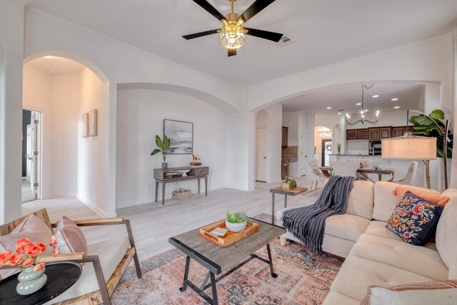 living area with arched walkways, crown molding, light wood finished floors, and ceiling fan