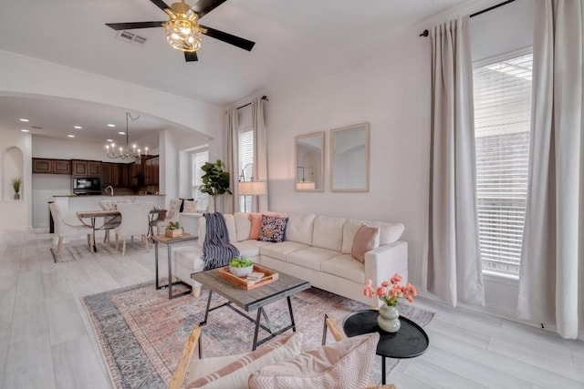 living room with arched walkways, light wood-style flooring, visible vents, and ceiling fan with notable chandelier