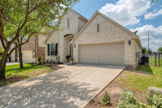 view of front facade featuring stone siding, an attached garage, driveway, and fence