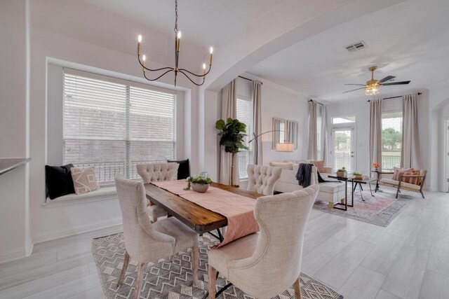dining area with visible vents, arched walkways, light wood-type flooring, baseboards, and ceiling fan with notable chandelier