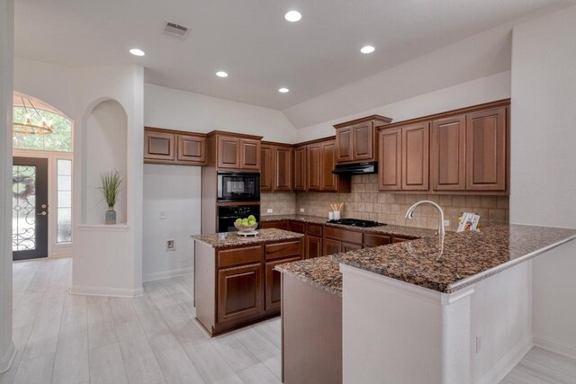 kitchen featuring under cabinet range hood, baseboards, dark stone counters, black appliances, and tasteful backsplash