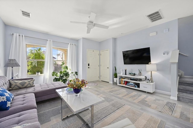 living area featuring light wood finished floors, baseboards, visible vents, and stairs