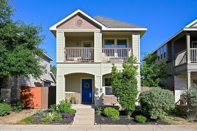 view of front of house featuring brick siding, fence, a balcony, and covered porch