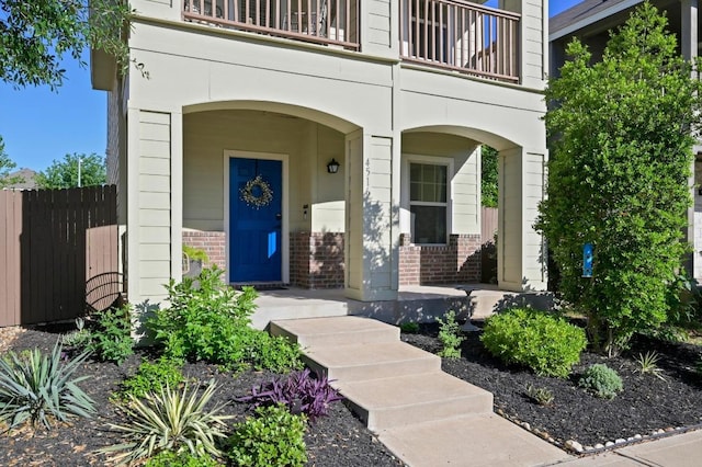 view of exterior entry featuring brick siding, a balcony, and fence
