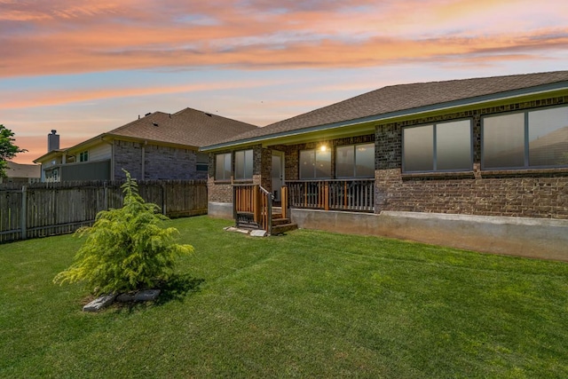 back of house at dusk with brick siding, fence, and a yard
