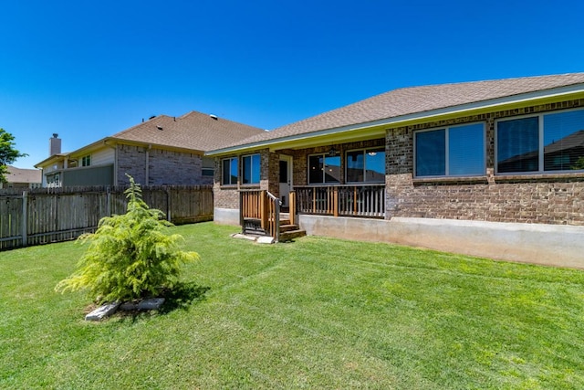 rear view of property featuring brick siding, a lawn, and fence