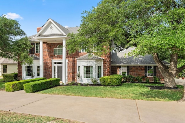 neoclassical home with brick siding, a front lawn, and a chimney
