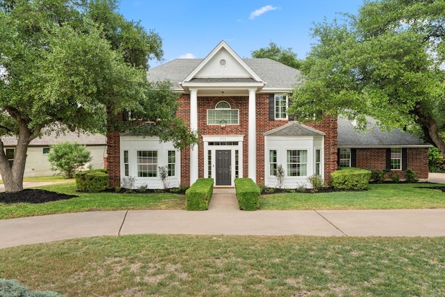 greek revival house with roof with shingles, brick siding, and a front yard
