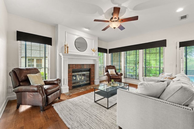 living area featuring a ceiling fan, visible vents, a fireplace, baseboards, and dark wood-style floors