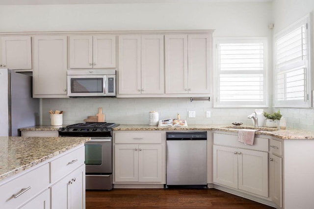 kitchen featuring dark wood-style flooring, appliances with stainless steel finishes, light stone counters, a sink, and backsplash