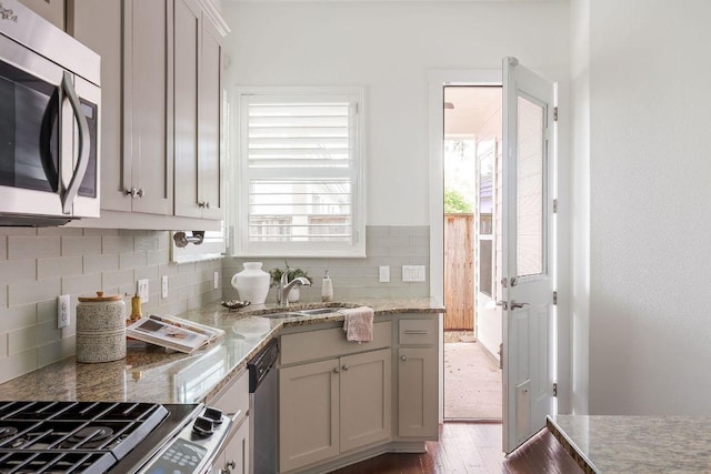 kitchen with appliances with stainless steel finishes, tasteful backsplash, wood finished floors, a sink, and light stone counters
