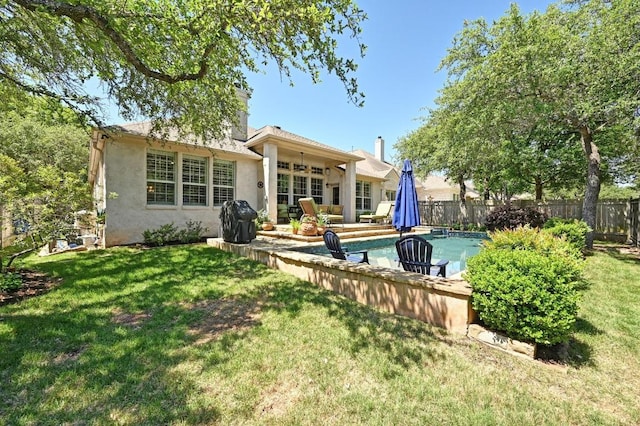 rear view of property featuring stucco siding, fence, a yard, and a fenced in pool