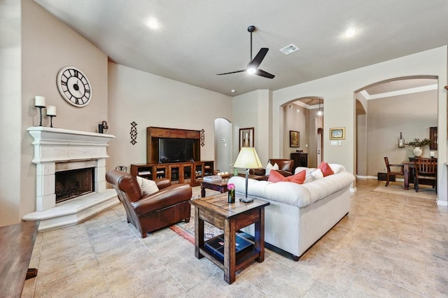 living area with arched walkways, a ceiling fan, a fireplace with raised hearth, and visible vents