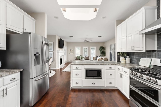 5710 Carry Back Ln, Austin, TX 78746 - kitchen featuring appliances with stainless steel finishes, wall chimney range hood, open floor plan, a peninsula, and white cabinetry