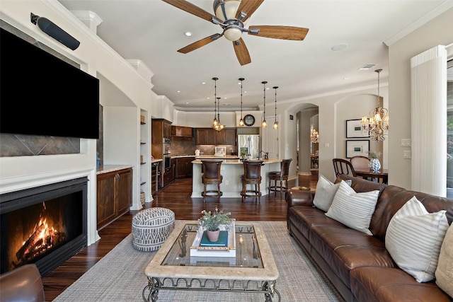 27435 Waterfall Hill Pkwy, Spicewood, TX 78669 - living room featuring dark wood finished floors, a lit fireplace, ceiling fan with notable chandelier, and arched walkways