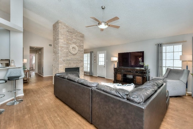 living room with ceiling fan, a textured ceiling, light wood-type flooring, and a fireplace