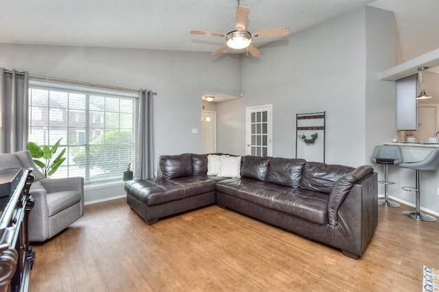 living area featuring a textured ceiling, ceiling fan, light wood-style floors, baseboards, and high vaulted ceiling