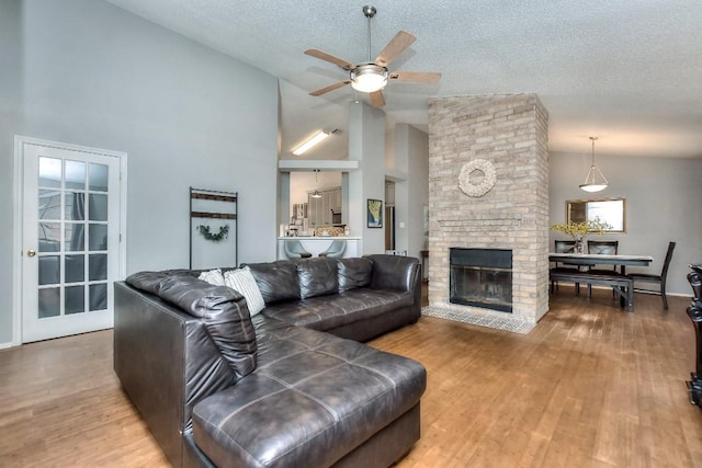 living area featuring a fireplace, high vaulted ceiling, a ceiling fan, a textured ceiling, and wood finished floors