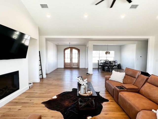 living area with lofted ceiling, a glass covered fireplace, visible vents, and light wood-style floors