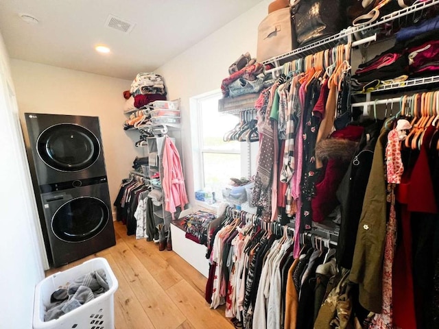 spacious closet with hardwood / wood-style floors, stacked washer and dryer, and visible vents
