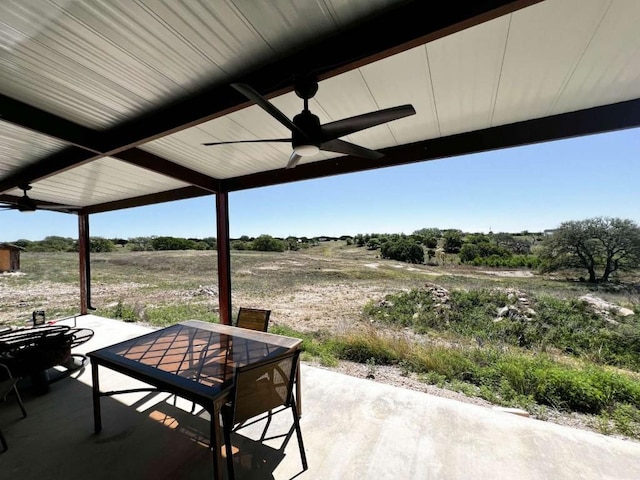 view of patio featuring outdoor dining area, a ceiling fan, and a rural view