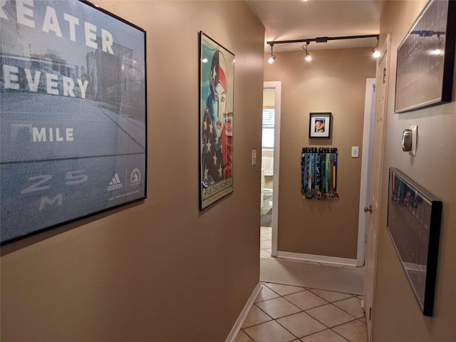 corridor featuring baseboards, rail lighting, and light tile patterned floors